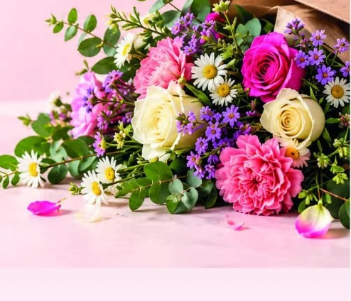 A letterbox bouquet of pink roses, carnations, daisies and purple flowers spilling from brown paper