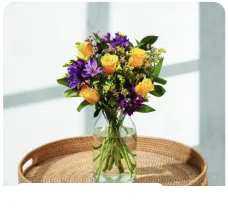 The Fairtrade Lydia bouquet of yellow roses and purple flowers in a glass vase