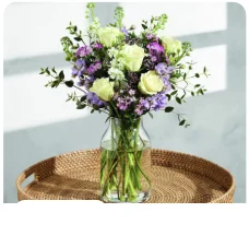 The Hallie bouquet of pale green roses and purple flowers in a glass vase