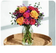 The Jade bouquet of orange roses, pink blooms and purple flowers in a glass vase